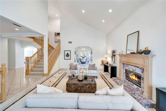 living room with visible vents, arched walkways, stairs, high vaulted ceiling, and a high end fireplace