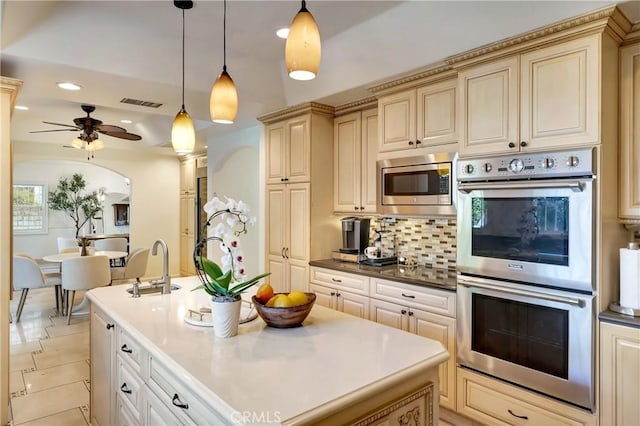 kitchen featuring a kitchen island with sink, stainless steel appliances, visible vents, cream cabinetry, and tasteful backsplash