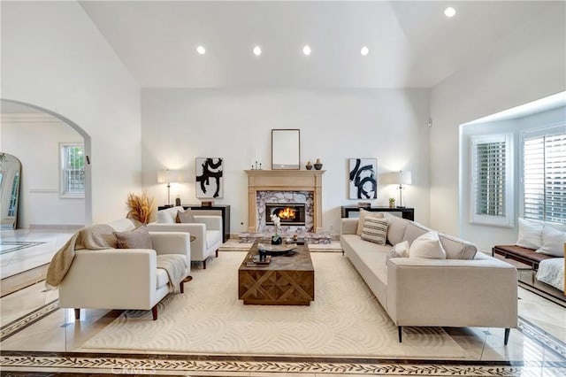 living area with arched walkways, a towering ceiling, a high end fireplace, and recessed lighting