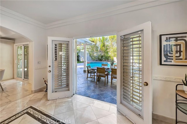 doorway to outside featuring arched walkways, ornamental molding, and baseboards