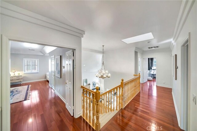 hallway with dark wood-style flooring, visible vents, a skylight, an upstairs landing, and a notable chandelier