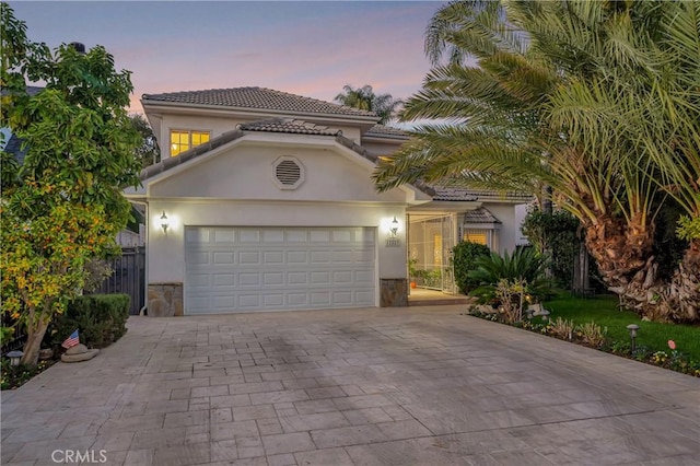 mediterranean / spanish-style house featuring a garage, decorative driveway, a tiled roof, and stucco siding