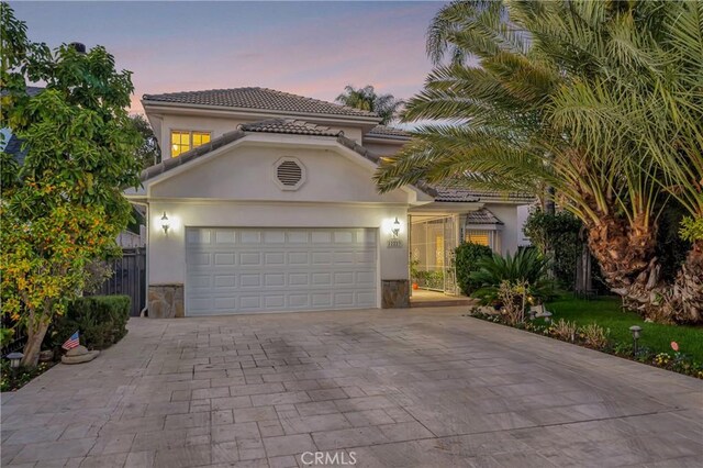 mediterranean / spanish-style home featuring a tile roof, stone siding, a garage, stucco siding, and driveway