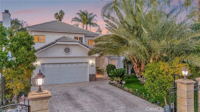 mediterranean / spanish home featuring a garage, a tiled roof, decorative driveway, and stucco siding