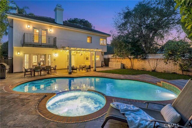 pool at dusk featuring french doors, a pool with connected hot tub, a fenced backyard, a patio, and outdoor dining space