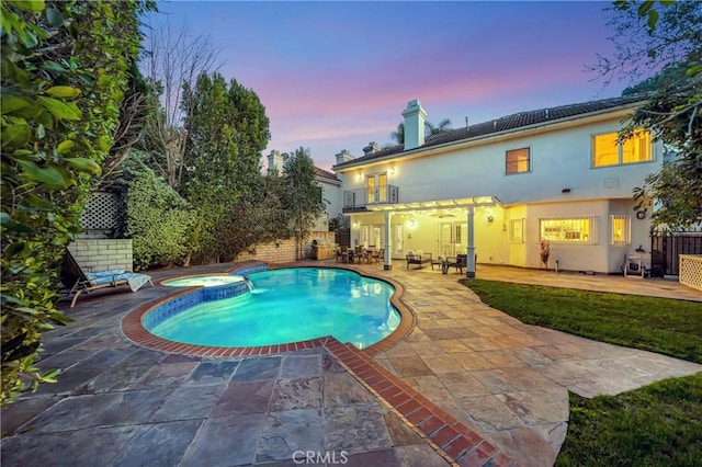 pool at dusk with a patio area, fence, and a pool with connected hot tub