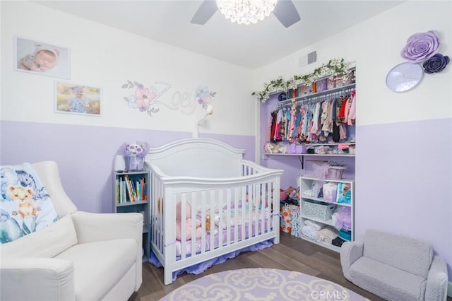 bedroom featuring ceiling fan, a crib, wood finished floors, and visible vents