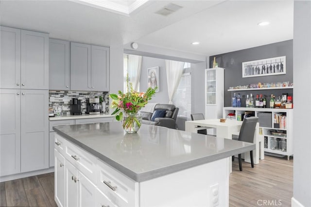 kitchen with wood finished floors, a kitchen island, visible vents, tasteful backsplash, and dark countertops