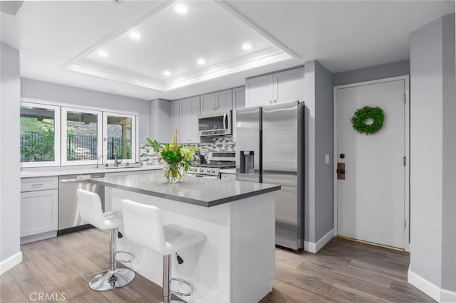 kitchen with a kitchen island, appliances with stainless steel finishes, a tray ceiling, light wood-type flooring, and a kitchen bar