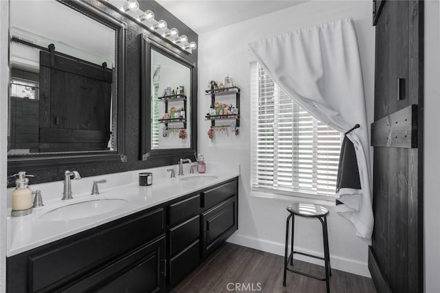 full bath featuring double vanity, a sink, baseboards, and wood finished floors