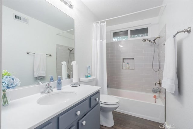 bathroom with toilet, wood finished floors, vanity, visible vents, and shower / tub combo with curtain