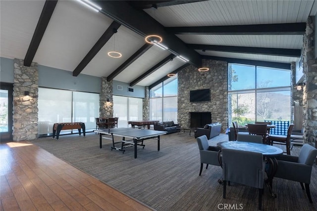 game room featuring high vaulted ceiling, wood finished floors, a wealth of natural light, and a stone fireplace