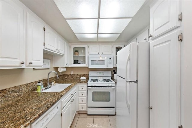 kitchen featuring white appliances, dark stone counters, white cabinets, a sink, and light tile patterned flooring