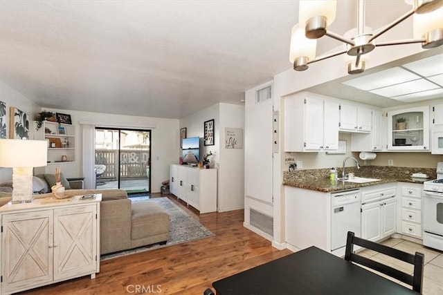 kitchen with white appliances, a sink, white cabinetry, dark stone countertops, and glass insert cabinets