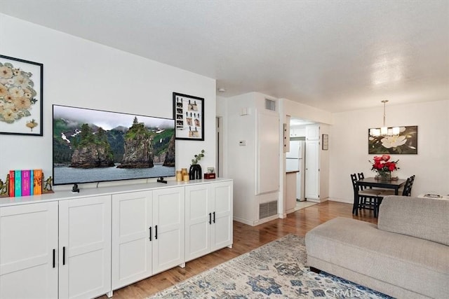 living area featuring light wood-style flooring, visible vents, and a notable chandelier