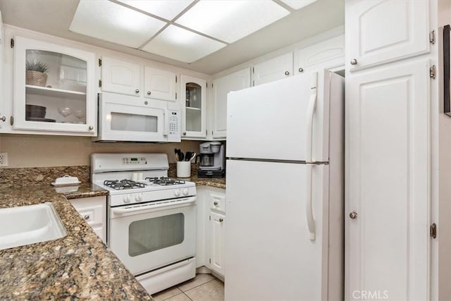 kitchen featuring dark stone counters, white appliances, white cabinetry, and light tile patterned floors