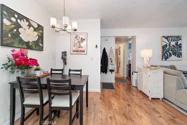 dining room with light wood-type flooring, a notable chandelier, and baseboards