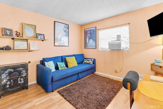 living area with a textured ceiling, cooling unit, wood finished floors, and baseboards