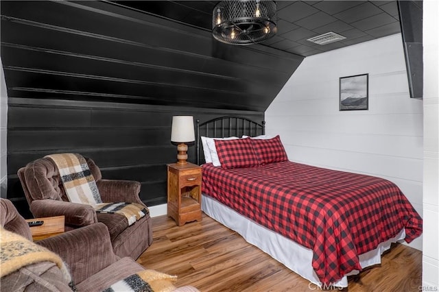 bedroom featuring lofted ceiling, visible vents, wooden walls, wood finished floors, and a chandelier