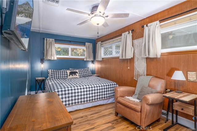 bedroom with visible vents, light wood-style flooring, and wooden walls