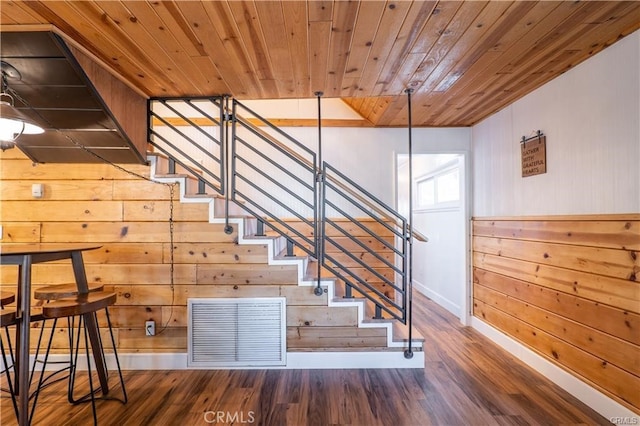 stairway with wooden walls, wood finished floors, wood ceiling, visible vents, and baseboards