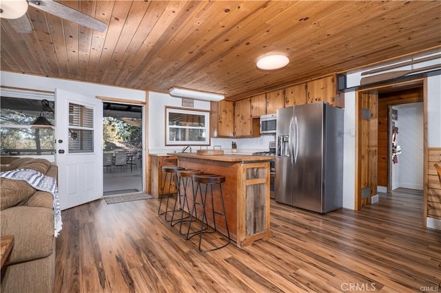 kitchen featuring stainless steel appliances, wood finished floors, a center island, brown cabinetry, and a kitchen bar