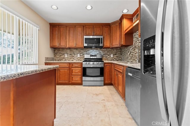 kitchen featuring light stone countertops, brown cabinetry, a sink, appliances with stainless steel finishes, and backsplash