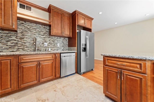 kitchen with visible vents, a sink, stainless steel appliances, brown cabinetry, and light stone countertops