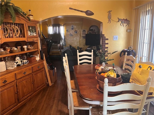 dining space featuring arched walkways and dark wood finished floors