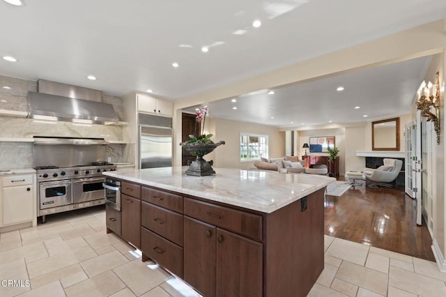 kitchen with high quality appliances, a center island, wall chimney range hood, backsplash, and recessed lighting