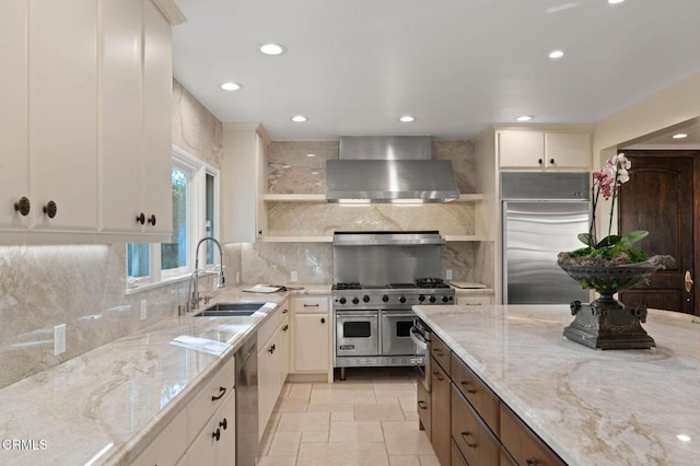 kitchen with open shelves, high end appliances, a sink, light stone countertops, and wall chimney exhaust hood