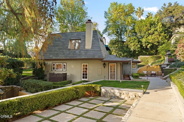 view of front facade with a chimney, mansard roof, a patio, and stucco siding