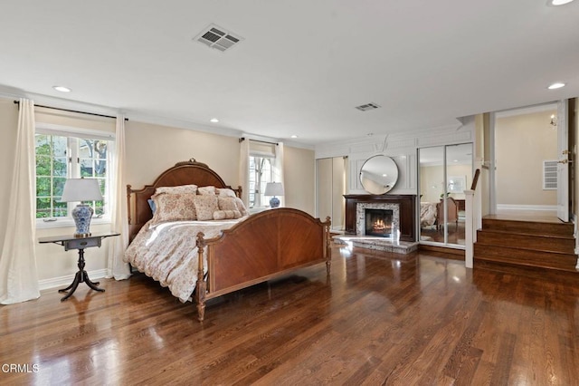 bedroom with a lit fireplace, wood finished floors, visible vents, and crown molding