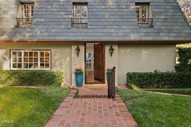 property entrance featuring mansard roof, a lawn, and stucco siding