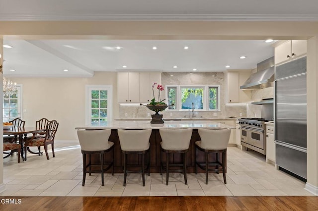 kitchen featuring a center island, light countertops, backsplash, high quality appliances, and wall chimney exhaust hood