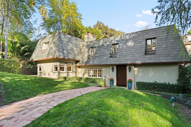 view of property with mansard roof, a chimney, a front yard, and stucco siding