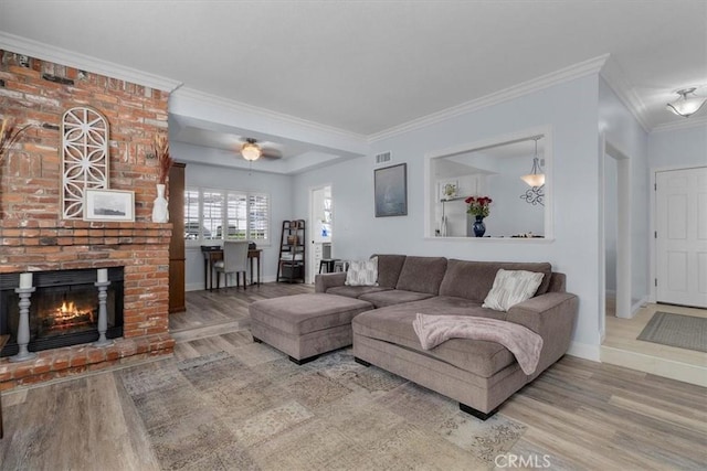 living room featuring a brick fireplace, baseboards, visible vents, and wood finished floors