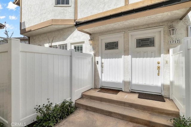 entrance to property featuring fence and stucco siding