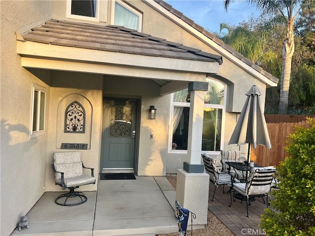 view of exterior entry featuring outdoor dining space, a tile roof, fence, and stucco siding