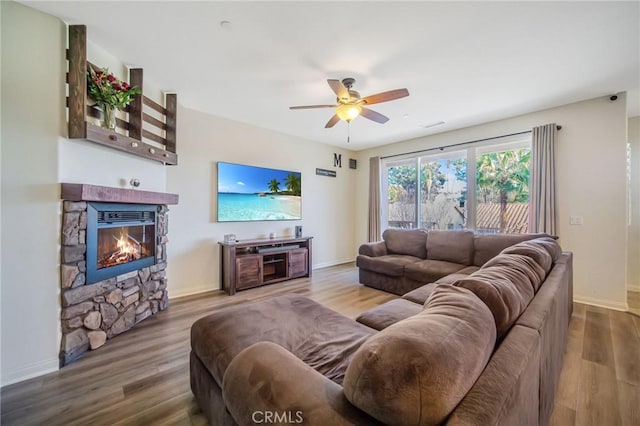 living area with a fireplace, wood finished floors, baseboards, and ceiling fan