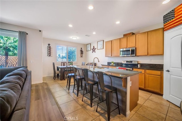 kitchen with open floor plan, a breakfast bar area, an island with sink, appliances with stainless steel finishes, and a sink