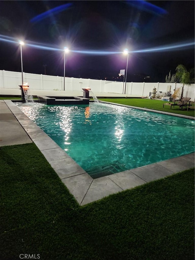 pool at night with a yard, a fenced backyard, and a fenced in pool