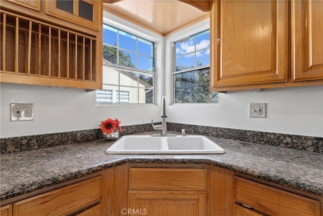 kitchen with brown cabinetry, dark countertops, and a sink