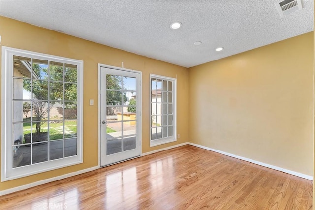 doorway with a wealth of natural light, visible vents, a textured ceiling, and light wood finished floors