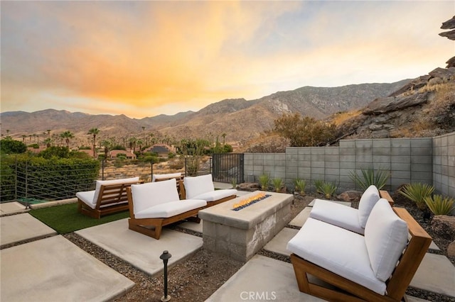 patio terrace at dusk with fence private yard, an outdoor living space with a fire pit, and a mountain view