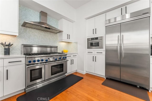 kitchen with light wood-style floors, white cabinets, light countertops, appliances with stainless steel finishes, and wall chimney exhaust hood