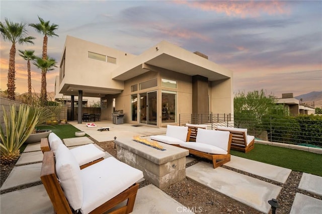 back of house at dusk with stucco siding, a patio area, an outdoor living space with a fire pit, and fence