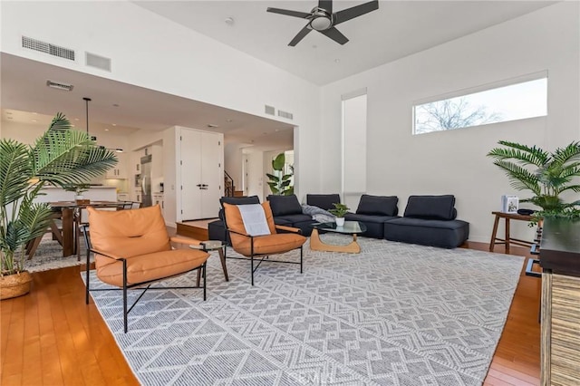 living room with stairway, ceiling fan, visible vents, and wood finished floors