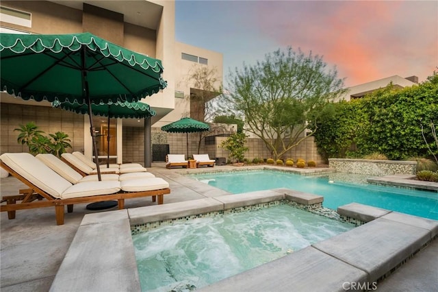 pool at dusk featuring an in ground hot tub, a patio, a fenced backyard, and a fenced in pool