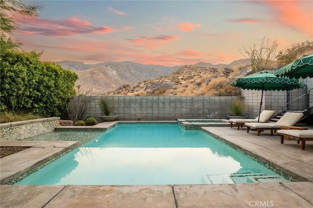 pool at dusk with a fenced backyard, a mountain view, an in ground hot tub, a fenced in pool, and a patio area